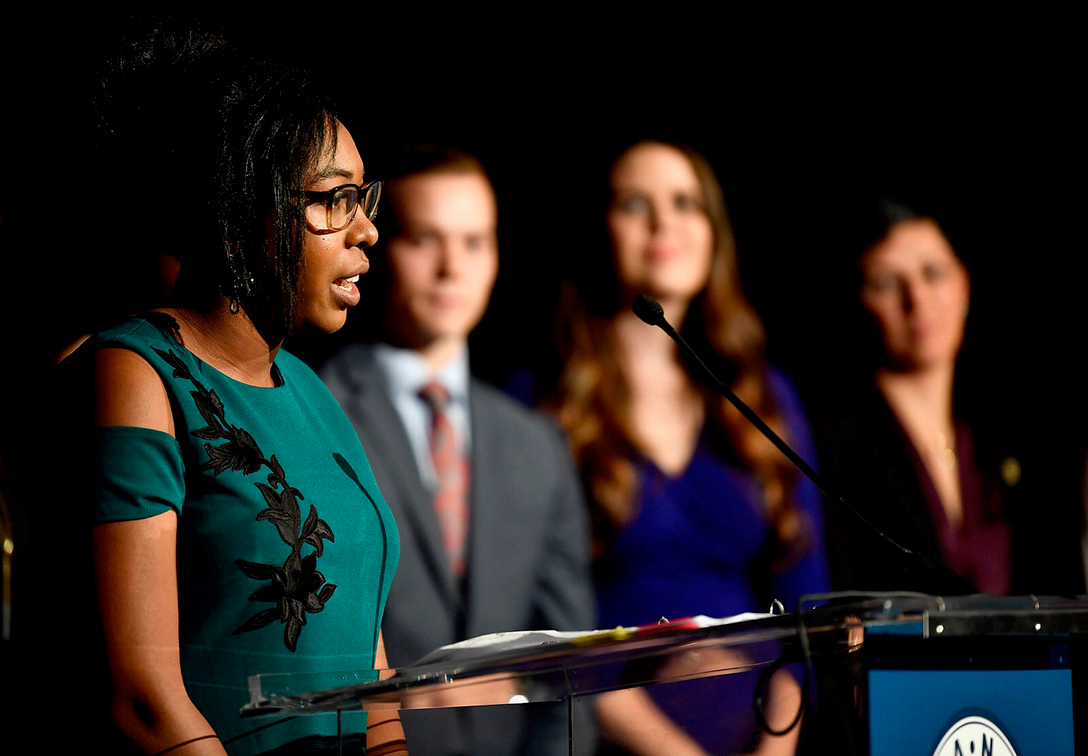 woman giving a speech on stage with others behind her