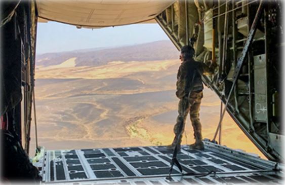 cargo plane with the back hatch down flying over mountains