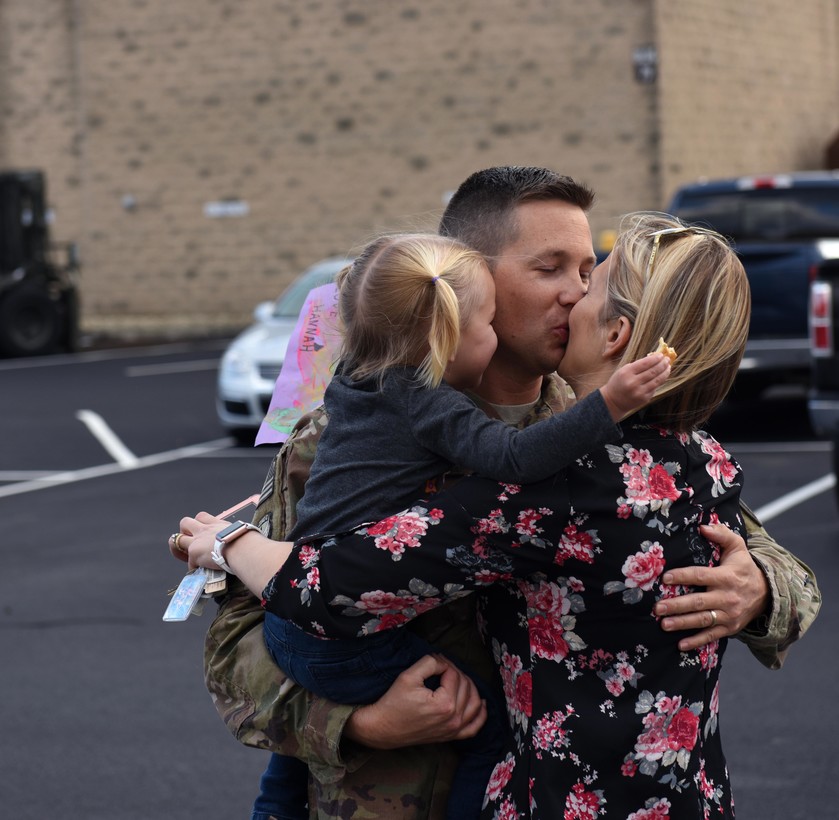 Service member holding his daughter and wife