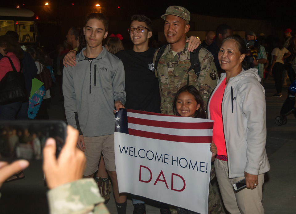Family holding a sign that says "Welcome Home DAD"